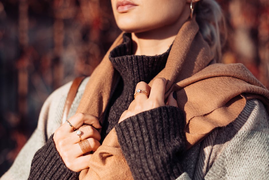 close up of woman's hands adjusting stylish scarf around neck, city background