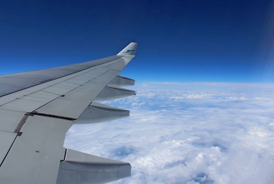 L'ala di un aereo visibile sopra le nuvole, con la terra sottostante, simboleggiando la rapidità e la capacità di coprire lunghe distanze del viaggio in aereo, ideale per "city breaks" europee.