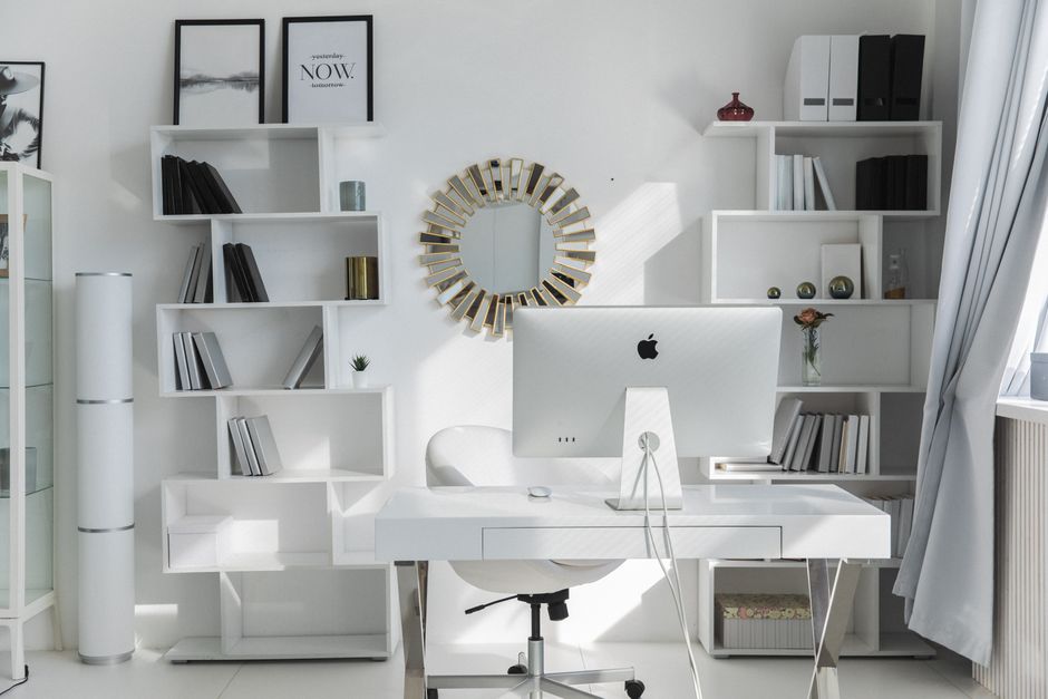 Un moderno spazio ufficio domestico luminoso e organizzato con una scrivania pulita, una sedia ergonomica e piante verdi. I cavi sono nascosti e gli oggetti sono ben sistemati per un ambiente di lavoro sereno.