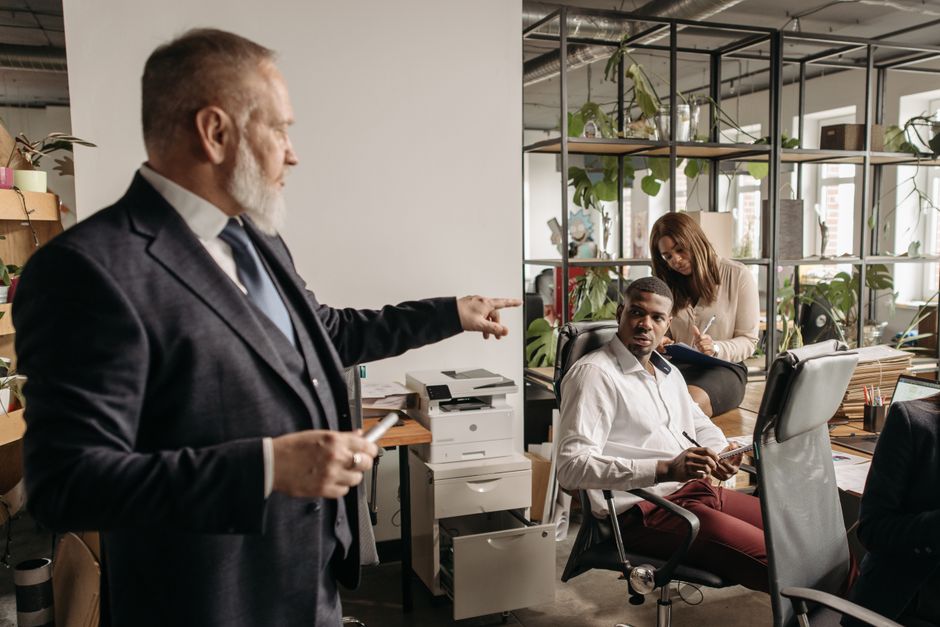 Un uomo d'affari dà istruzioni chiare e precise a un team di colleghi in un moderno ufficio, rappresentando l'efficacia dei prompt per il lavoro nelle interazioni umane.