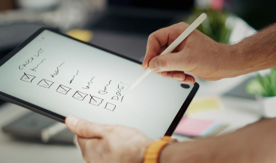 Tablet se zobrazeným kontrolním seznamem a rozmazaným pozadím elektroniky jako notebooky a chytré hodinky.