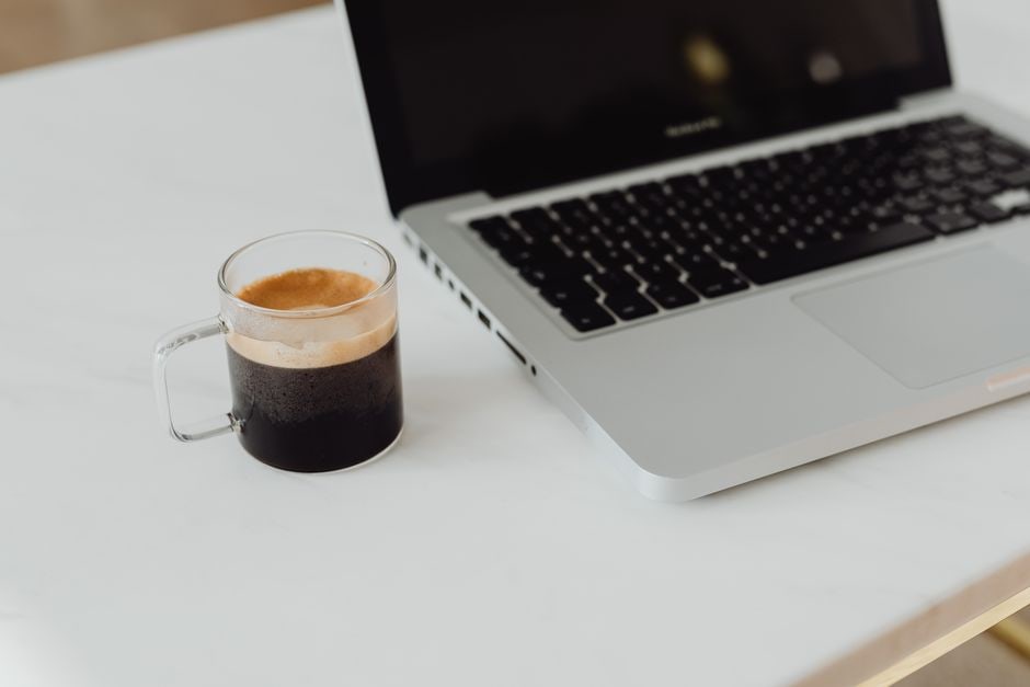 Rituale del caffè mattutino con una tazza da viaggio e un laptop su un tavolo, che rappresenta la routine lavorativa e personale in movimento.