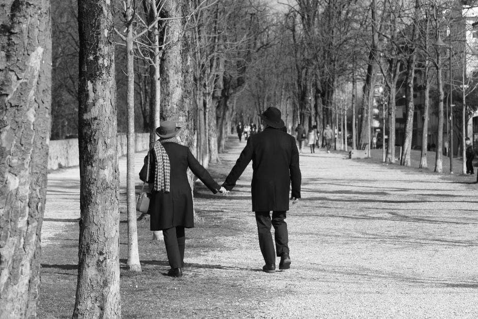 Coppia che passeggia mano nella mano in un parco cittadino sotto il sole, rappresentando la connessione e il relax durante il weekend.