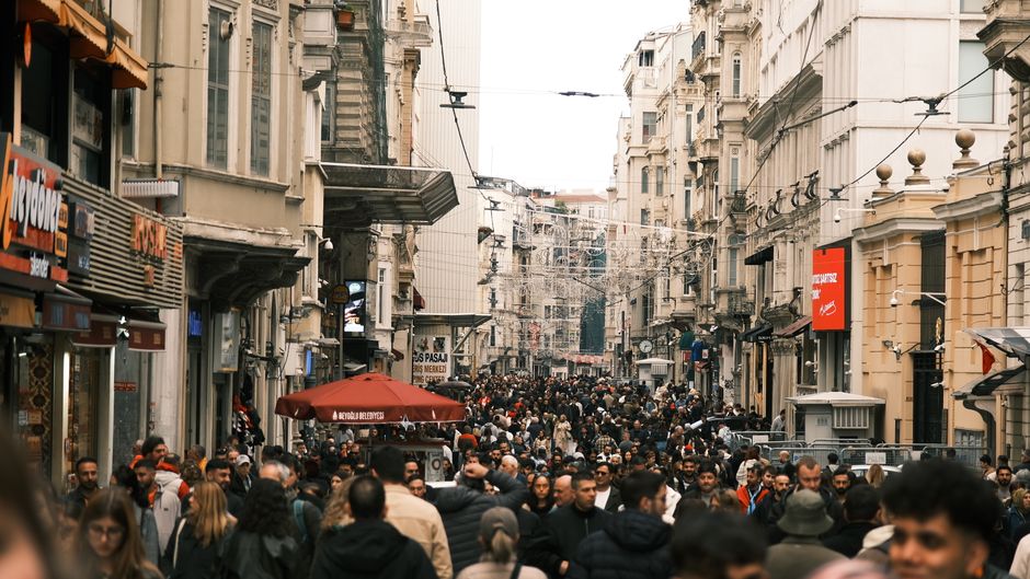 Una strada storica affollata di persone che camminano, in una città europea, con edifici antichi e negozi tradizionali ai lati, trasmettendo un senso di movimento costante.