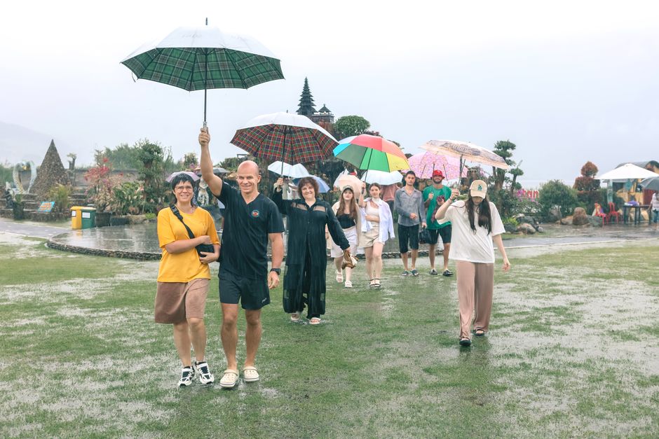 Un gruppo eterogeneo di turisti con ombrelli colorati passeggia sotto la pioggia in una strada cittadina europea, dimostrando la resilienza nel godersi il viaggio nonostante il maltempo.