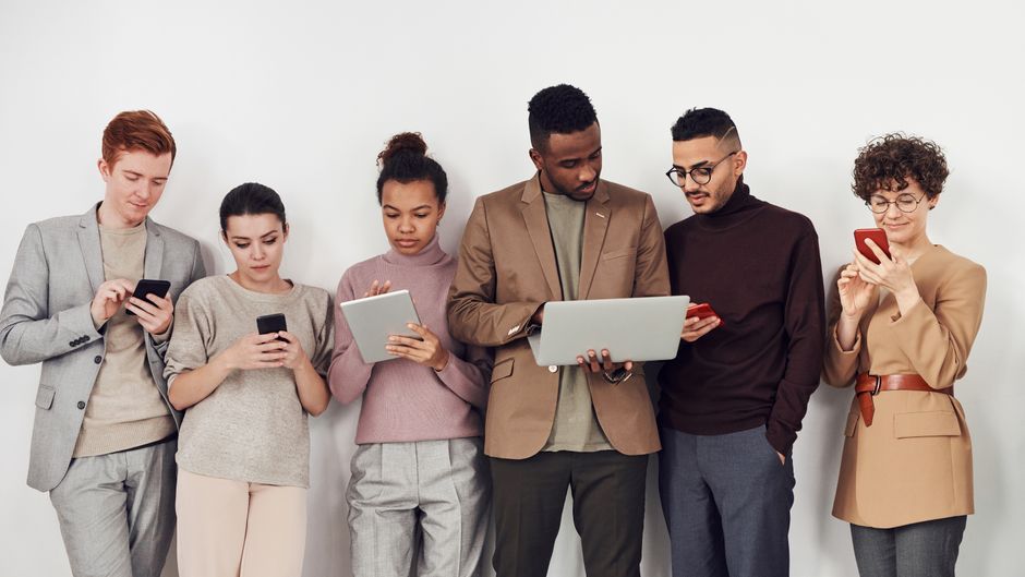 Diverse persone di età e etnie differenti che interagiscono con computer portatili, smartphone e schermi touch, usando vari strumenti AI