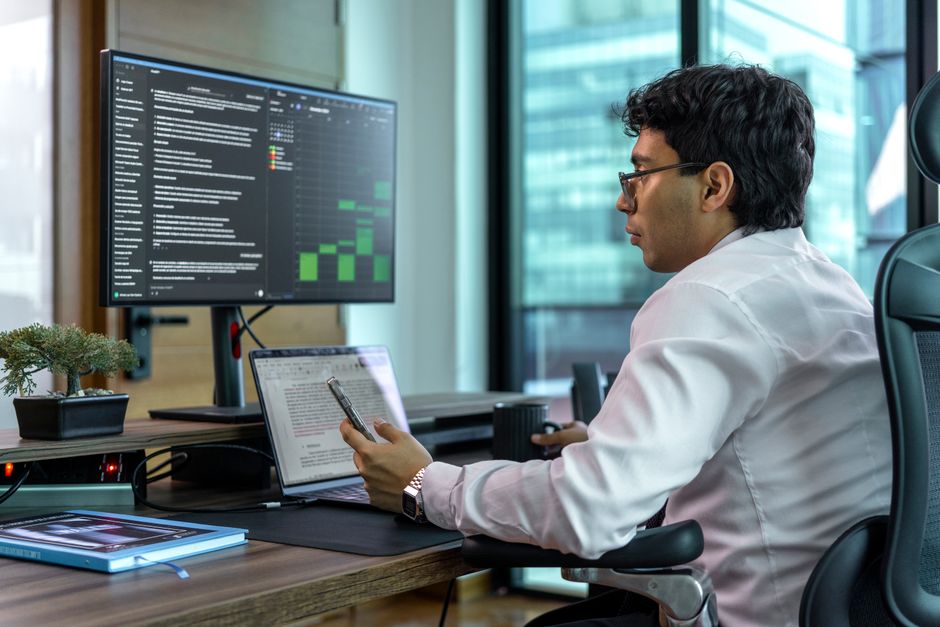 Un setup con due monitor su una scrivania in un appartamento piccolo, uno schermo mostra un'email di lavoro e l'altro una piattaforma di streaming, simboleggiando la separazione virtuale.