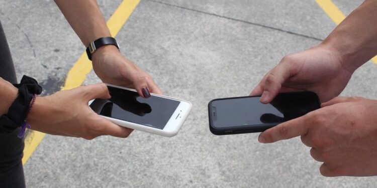 Una famiglia seduta sul divano, con i genitori che consultano offerte di piani telefonici su un tablet mentre i figli usano i loro smartphone.