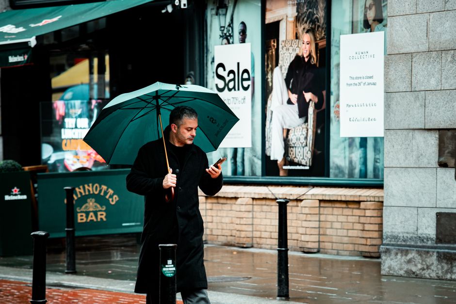 Uomo d'affari che controlla le previsioni meteo sul telefono, simbolo dell'importanza della pianificazione stagionale per l'outfit di viaggio.