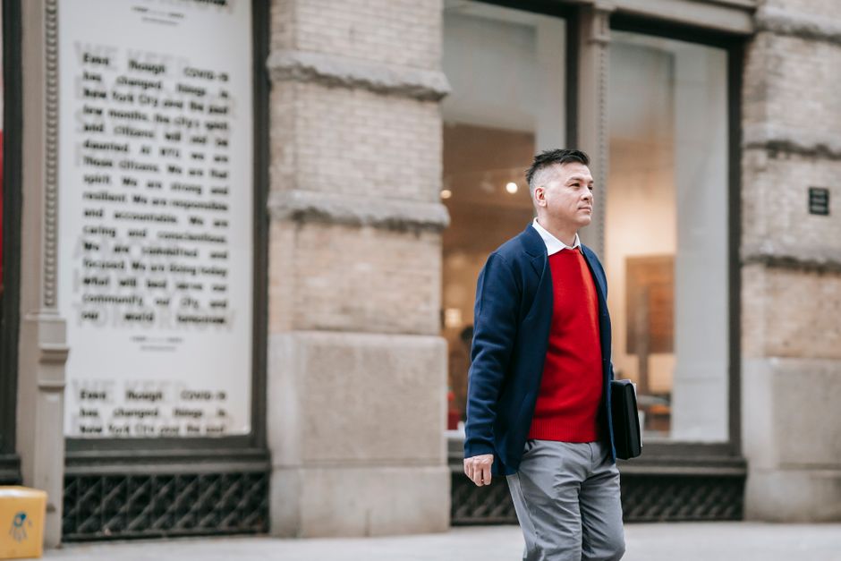Мужчына ў стылі smart casual ідзе па гістарычным цэнтры еўрапейскага горада, атрымліваючы асалоду ад шпацыру.