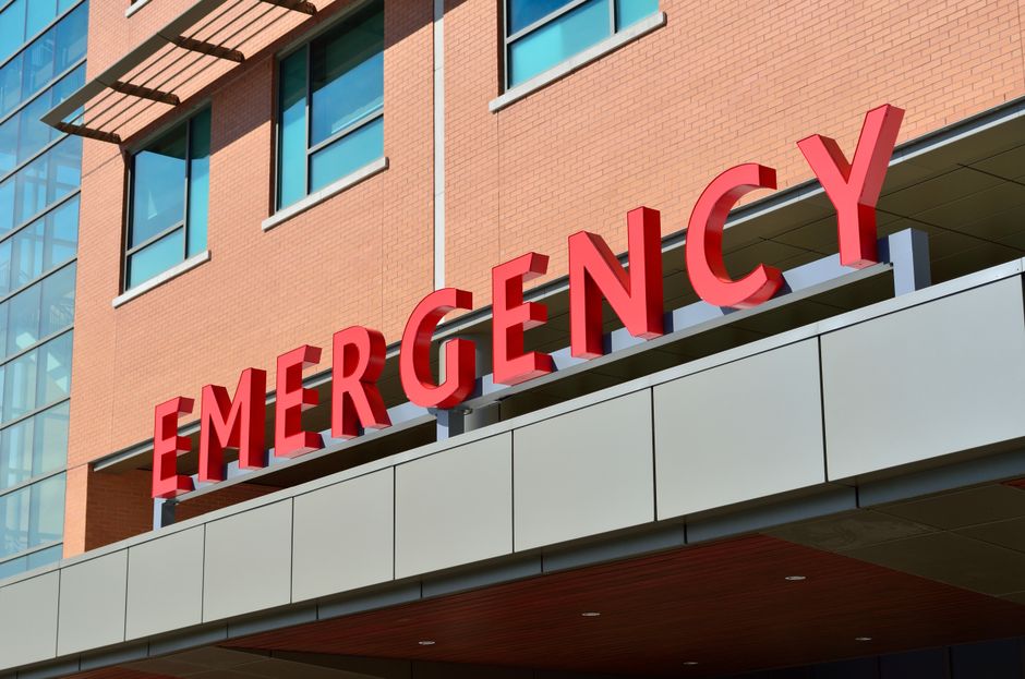 Un medico con stetoscopio e mascherina parla con una persona in un letto d'ospedale, indicando un laptop per il teleconsulto.