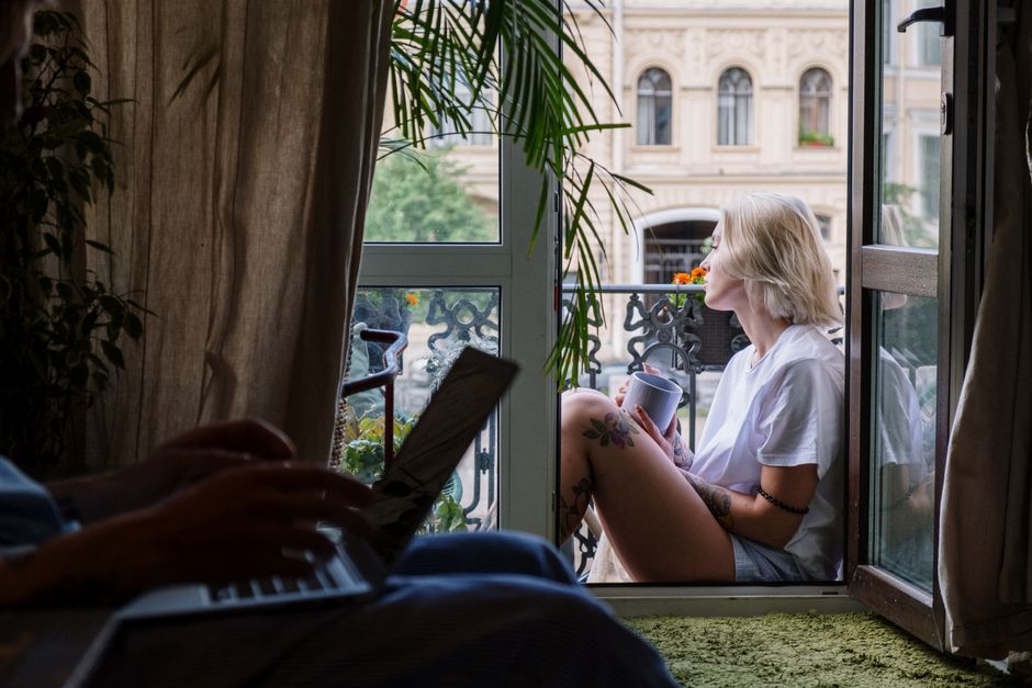 Muž si vychutnává ranní kávu na malém balkóně s výhledem na městskou zástavbu.