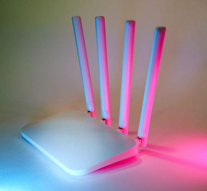 Un moderno router Wi-Fi bianco con antenne visibili, circondato da cavi Ethernet colorati su una scrivania, a indicare una rete domestica ottimizzata.
