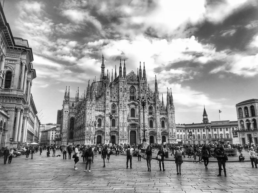 Visitatori con spalle coperte che ammirano silenziosamente l'interno maestoso di una cattedrale gotica europea.
