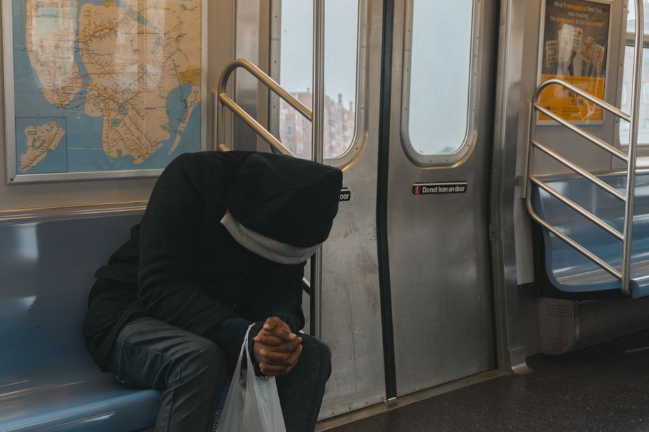 Un uomo con uno zaino, stanco, scende da un treno affollato a Milano durante l'ora di punta serale.