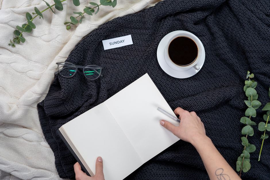 Una persona che beve caffè e scrive su un quaderno la domenica mattina, con luce calda e piante