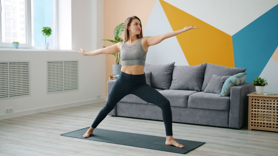 Una persona che pratica yoga in un piccolo spazio pulito e ben organizzato, dimostrando come mantenere le abitudini di benessere.