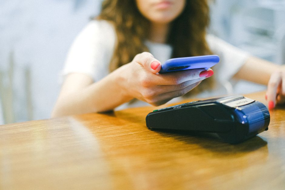 Рука трымае смартфон для аплаты праз NFC на плацежным тэрмінале ў замежным магазіне.