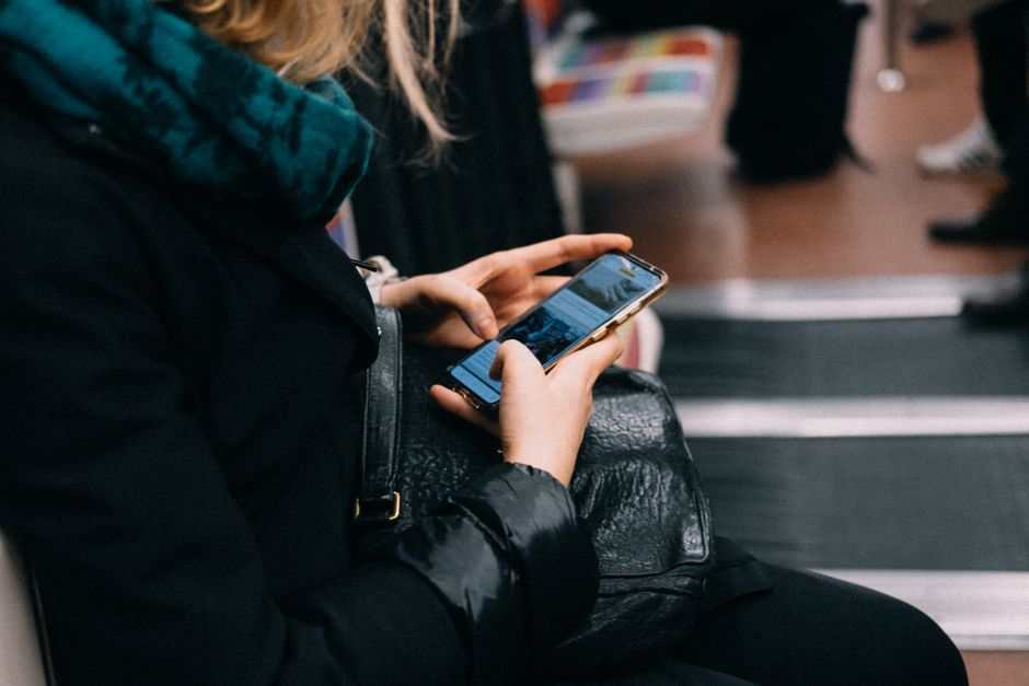 Una persona che tiene in mano uno smartphone che funge da hotspot, con un laptop aperto sullo sfondo in un ambiente come un treno o una caffetteria, per connettività in viaggio.