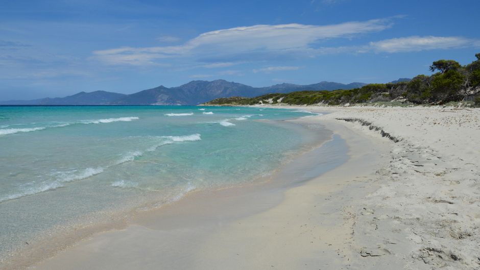Spiaggia sabbiosa nel Sud Italia con mare calmo e pochi bagnanti al tramonto.
