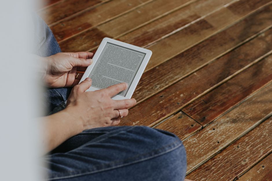 Un lavoratore remoto legge un e-reader sul balcone del suo appartamento in città, godendosi un momento di relax.