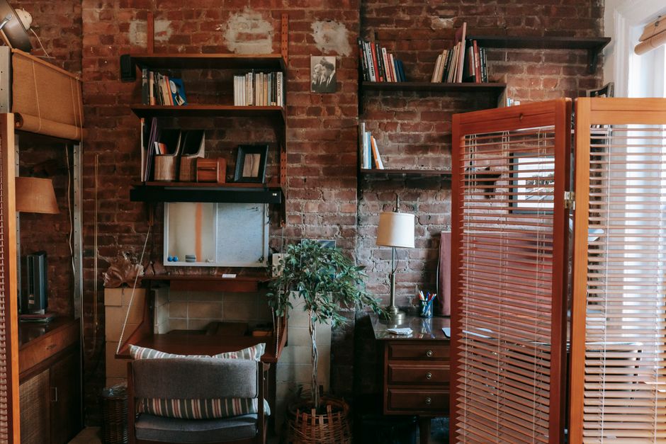 Una libreria a giorno con piante e libri, che funge da divisorio tra due aree di un piccolo appartamento, garantendo privacy visiva.