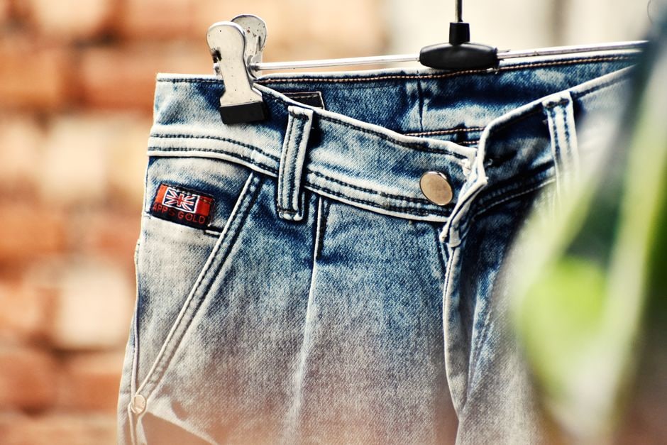 Un uomo indossa jeans slim-fit blu scuro, camicia bianca e blazer grigio, camminando in un ambiente urbano, ideale per un look smart casual.