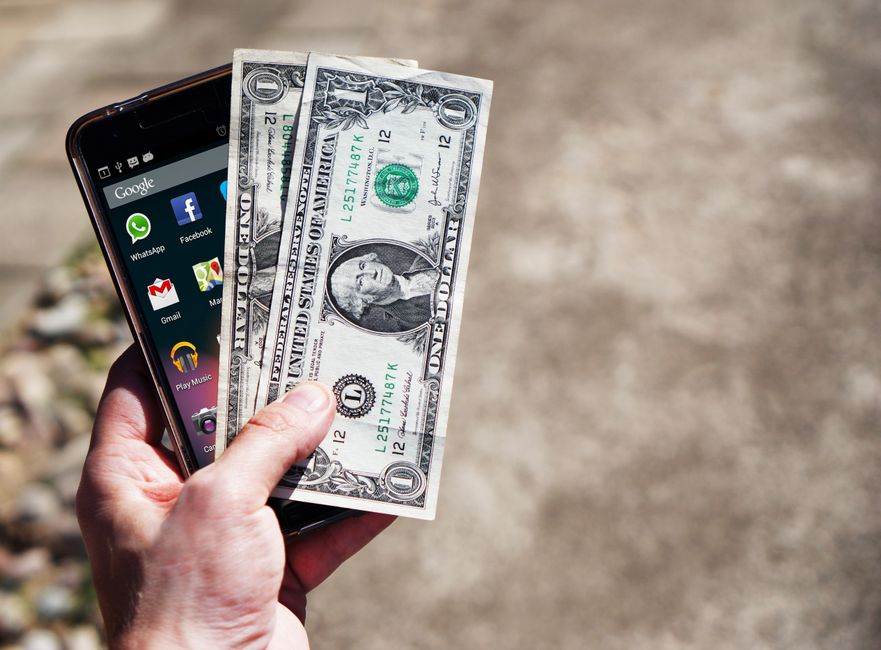 Schermo di uno smartphone che mostra l'interfaccia di un'app di pagamento multi-valuta con grafici e saldi, poggiato su una mappa geografica.