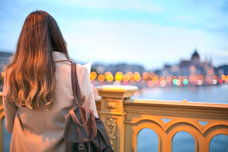 Donna che esplora una strada affascinante di una città europea, sorridendo mentre guarda una mappa digitale sul telefono, circondata da architetture storiche e negozietti tipici.