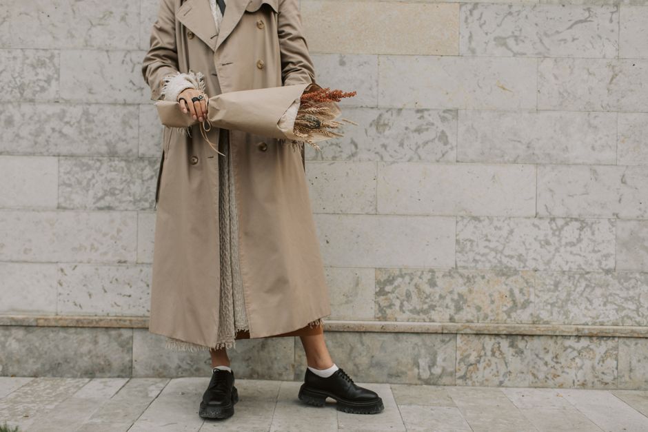 Un uomo in trench e jeans, con sneakers impermeabili, cammina su un marciapiede bagnato, portando una borsa a tracolla resistente all'acqua.