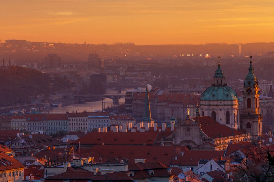 Klidné ranní slunce vychází nad střechami historických budov v Praze.