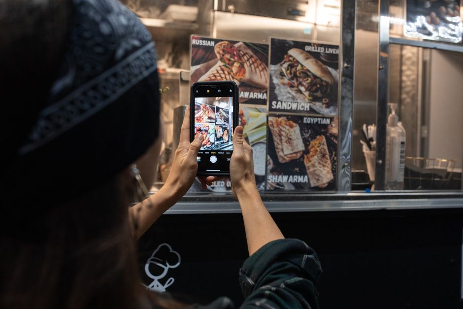 Primo piano di una mano che tiene uno smartphone puntato su un menù di un ristorante, mostrando la traduzione istantanea tramite fotocamera.