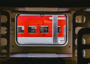 Interno di un treno moderno con un passeggero che guarda fuori dal finestrino il paesaggio italiano che scorre, evidenziando il comfort del viaggio in treno per brevi distanze in Italia.