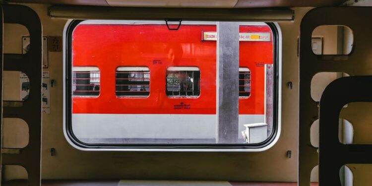Interno di un treno moderno con un passeggero che guarda fuori dal finestrino il paesaggio italiano che scorre, evidenziando il comfort del viaggio in treno per brevi distanze in Italia.