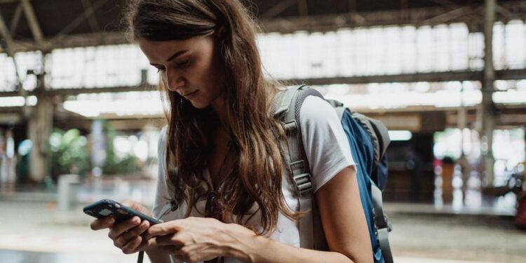 Viaggiatore italiano che controlla lo smartphone con una mappa dell'Europa sullo sfondo, mostrando preoccupazione per il roaming.