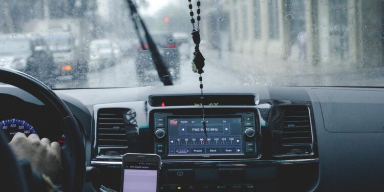 Un viaggiatore frustrato guarda il telefono mentre la pioggia cade fuori dalla finestra, simboleggiando la delusione delle previsioni meteo inaffidabili.