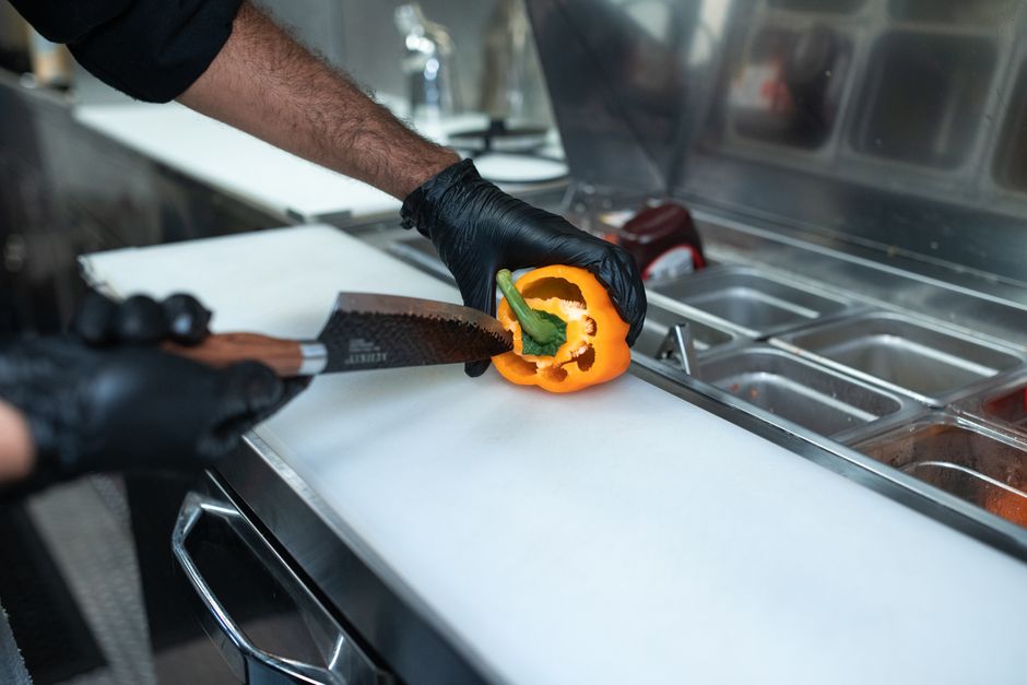 Mani che affettano verdure fresche su un tagliere in una cucina moderna e piccola