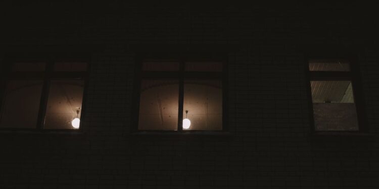Finestra di un appartamento urbano di notte, con luci della città in lontananza, simboleggiante l'inquinamento luminoso.