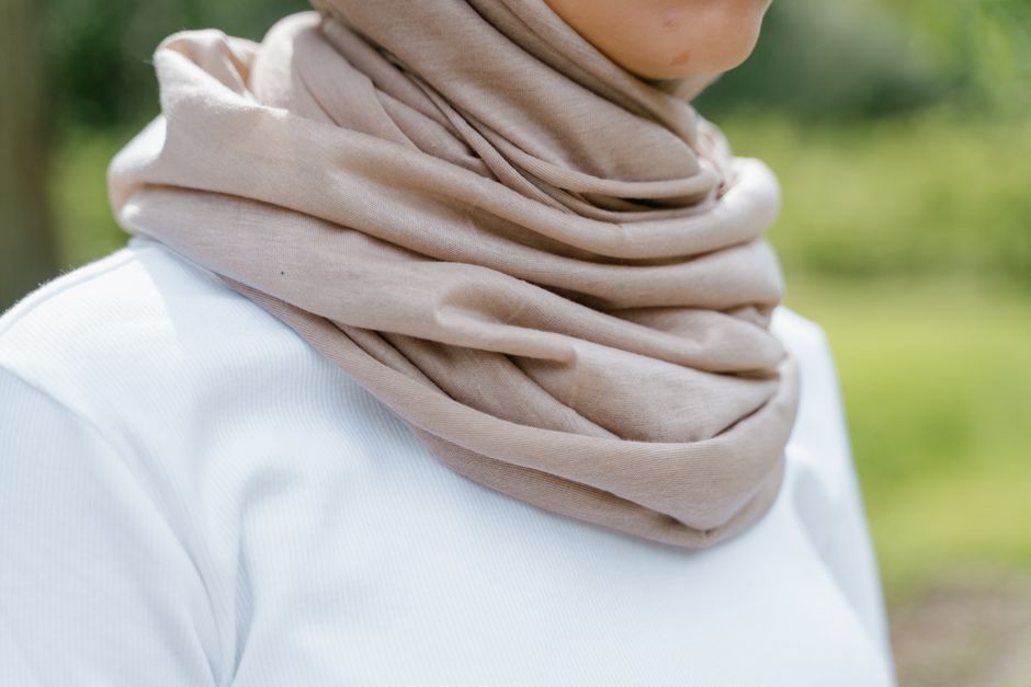 Dettaglio di un foulard in seta con fantasia vivace indossato in tre modi diversi: come sciarpa, fascia per capelli e cintura su un jeans
