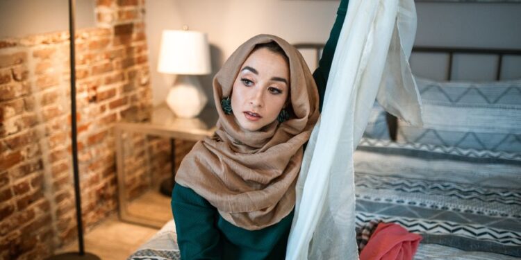 Donna sorridente che organizza accessori da viaggio, come foulard e gioielli, su un letto, con una valigia aperta sullo sfondo