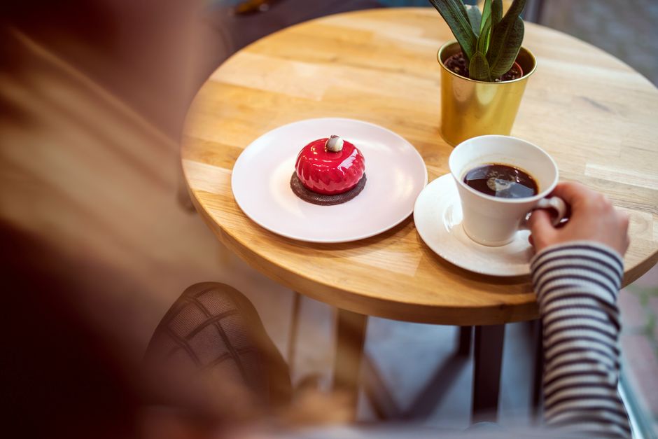 Viaggiatrice sola seduta in un accogliente caffè di una città italiana, gustando un cappuccino e scrivendo sul suo diario di viaggio, con un'atmosfera rilassata e autentica.