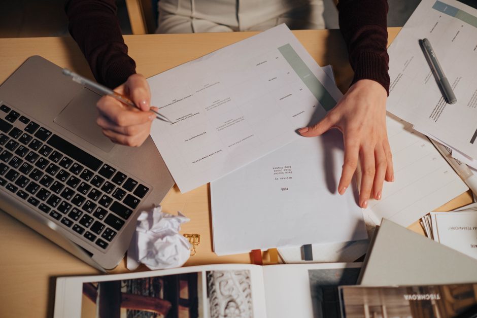 Una donna sta organizzando una scrivania disordinata, raggruppando carte, cavi e forniture per ufficio. Mostra il processo di decluttering attivo e di messa in ordine per una casa più calma.
