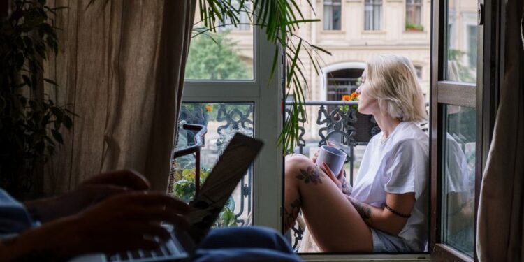 Donna che si rilassa su un balcone con una tazza di caffè, godendosi la calma mattutina, simbolo di un weekend rigenerante.