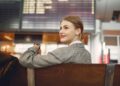 Donna elegante in aeroporto, con abiti smart casual e valigia a mano.