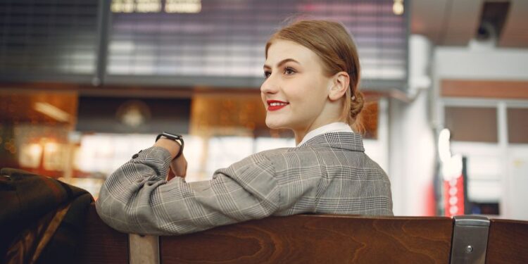 Donna elegante in aeroporto, con abiti smart casual e valigia a mano.