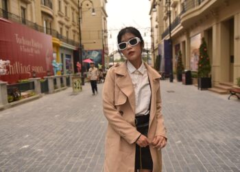 Donna con un trench beige che cammina in una città europea in primavera.