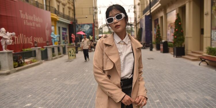 Donna con un trench beige che cammina in una città europea in primavera.