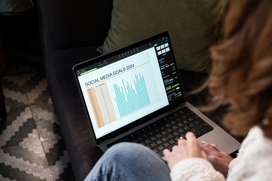 Una donna content creator sorridente che lavora al computer portatile, con icone di social media che fluttuano sullo schermo, mostrando efficienza nell'automazione.