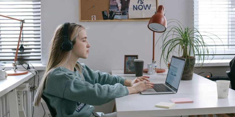 Donna italiana concentrata che lavora al computer in un ambiente domestico luminoso, con un caffè sul tavolo.