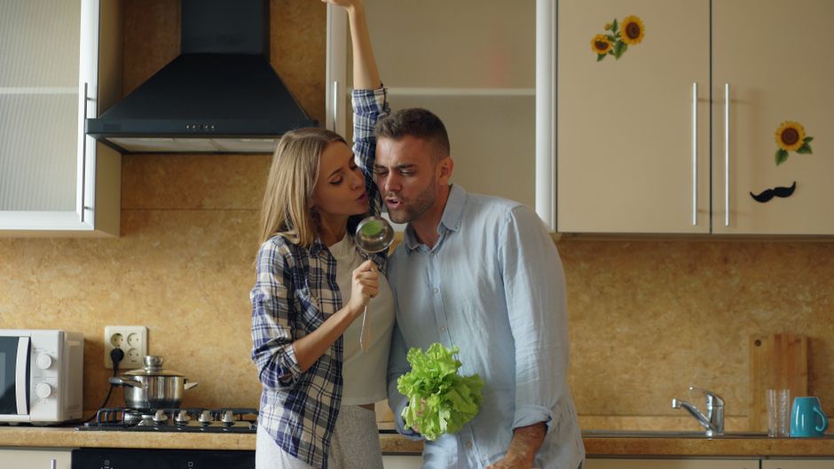 Giovani che cucinano in un appartamento durante un viaggio, con prodotti freschi sul tagliere.